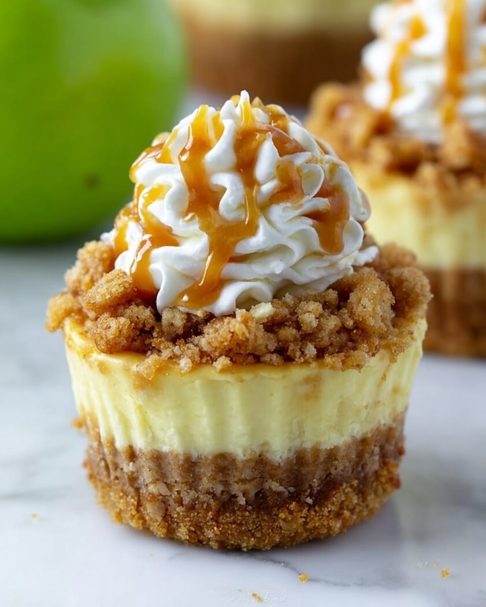 A close-up of a cupcake with four visible layers placed on a white marbled surface: the bottom layer is a crumbly, light brown crust; above it is a thick, smooth, pale yellow cream layer; on top of the cream is a chunky, golden brown crumb topping; the final layer is a swirl of white whipped cream with light brown caramel sauce drizzled over it. A green apple is blurred in the background. Photo taken with an iphone --ar 4:5 --v 7