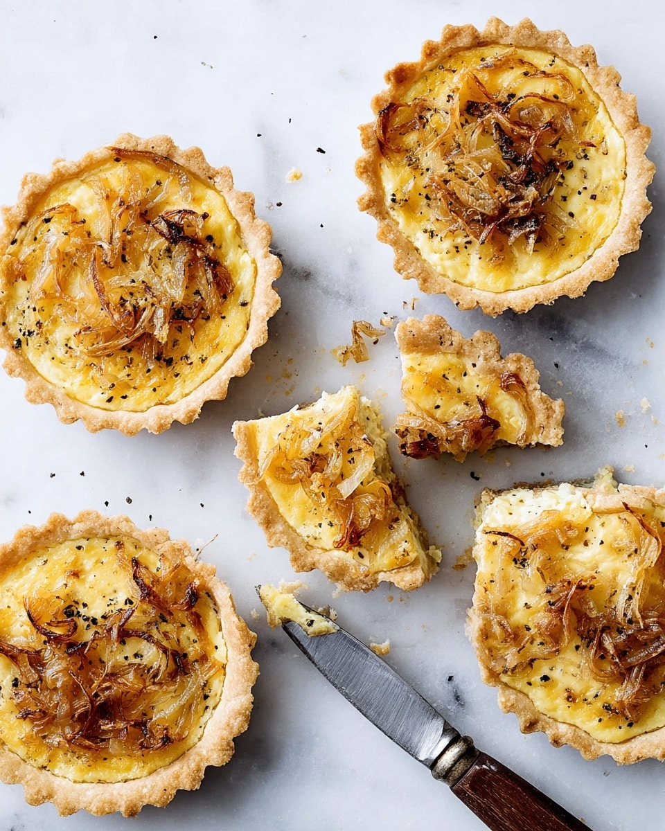 The image shows five small round tarts with a golden crust that is fluted around the edges. Each tart has one main layer filled with a creamy, slightly yellow mixture topped with caramelized onions that are golden brown and slightly crispy in parts. Some tarts are sprinkled lightly with cracked black pepper, adding texture and contrast. Two of the tarts are cut in half, showing the same creamy filling inside. A knife with a wooden handle and silver blade lies between the cut tarts on a white marbled surface. photo taken with an iphone --ar 4:5 --v 7