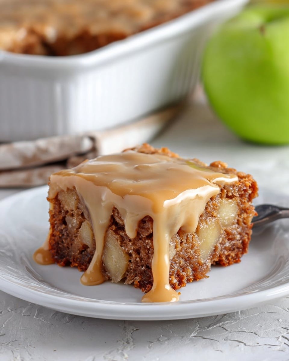 The image shows a square piece of apple cake on a white plate. The cake has three layers: a brown crumbly base with visible chunks of apple, a middle layer with more soft apple pieces mixed in, and a thick light caramel-colored glaze dripping over the top and sides. Near the plate, there is a gold and black fork resting on a white cloth. In the background, a white baking dish with the rest of the cake is placed on a white marbled surface. Three apples—two red and one green—are next to the baking dish, with a hexagon-tile patterned wall behind them. photo taken with an iphone --ar 4:5 --v 7