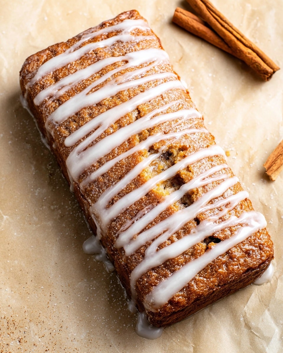 A rectangular brown cake with a rough texture is placed on a light tan surface with a white marbled finish. The cake has a drizzle of white icing forming irregular horizontal stripes across the top and sides, giving it a glossy and slightly wet look. The cake appears dense with a few small visible dark spots embedded inside. Two cinnamon sticks lie diagonally in the top right corner of the image on the white marbled surface. photo taken with an iphone --ar 4:5 --v 7