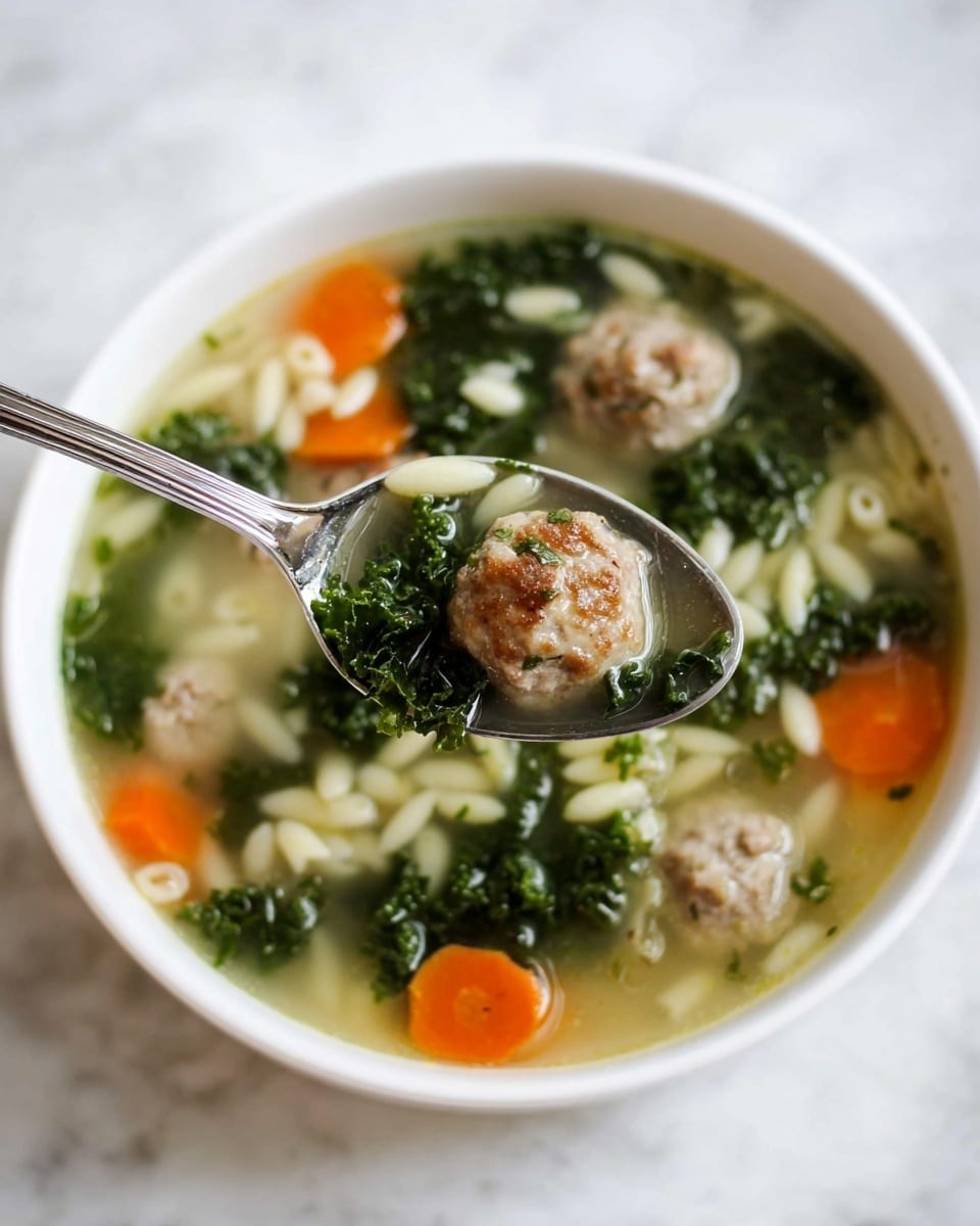 The image shows a white bowl filled with clear broth soup that has small meatballs, bright orange carrot slices, dark green leafy kale, and tiny cream-colored pasta pieces floating in it. A silver spoon holds one small meatball, a piece of carrot, kale, and pasta, hovering above the bowl. The soup layers include the clear, slightly oily broth visible at the top, followed by an even spread of the meatballs, kale, carrots, and pasta all mixed together. The bowl sits on a white marbled surface. photo taken with an iphone --ar 4:5 --v 7