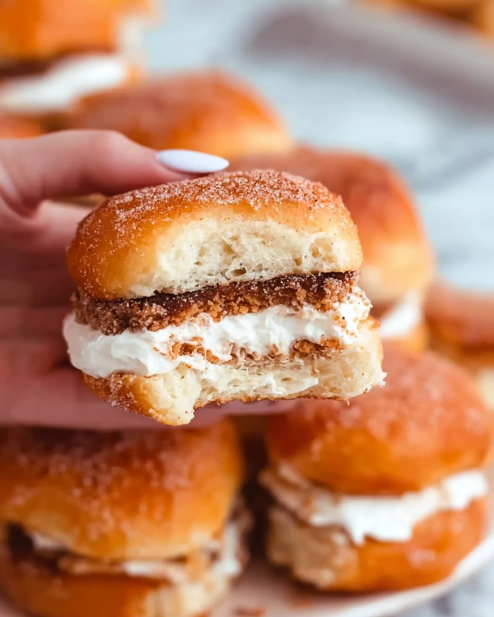 A close-up of a small sandwich held by a woman's hand, showing three clear layers: a top golden-brown soft bun sprinkled with sugar, a middle crispy textured brown layer of fried patty, and a bottom layer of smooth white cream filling spread between the bun halves. The sandwich is set against a blurred pile of similar sandwiches with the same golden buns and white cream peeking out. The background is a white marbled texture. photo taken with an iphone --ar 4:5 --v 7