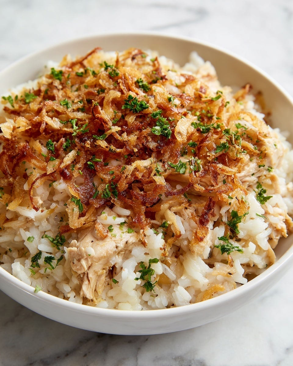 A close-up view of a creamy rice dish served in a white bowl, showing three main layers: the bottom layer is soft and lightly colored cooked rice, the middle layer has tender pieces of light brown chicken mixed throughout, and the top layer is a golden-brown, crispy onion topping scattered with small, bright green parsley flakes. The rice looks moist and slightly shiny, while the crispy onions add texture and richness. The bowl sits on a white marbled surface. photo taken with an iphone --ar 4:5 --v 7