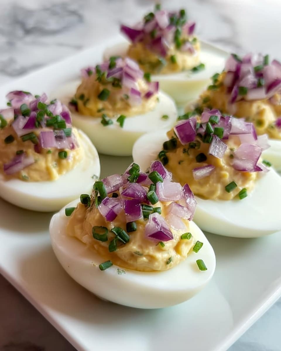 The image shows six deviled eggs placed on a white square plate resting on a white marbled surface. Each egg is halved, revealing a smooth, white outer layer filled with a creamy, pale yellow yolk mixture that is slightly textured. On top of the yolk filling are layers of finely chopped purple-red onions and small green chive pieces scattered evenly to add color contrast. The eggs are arranged close together, with the front egg in sharp focus, showing the creamy filling and fresh garnish clearly, while the eggs in the back are softly blurred. photo taken with an iphone --ar 4:5 --v 7