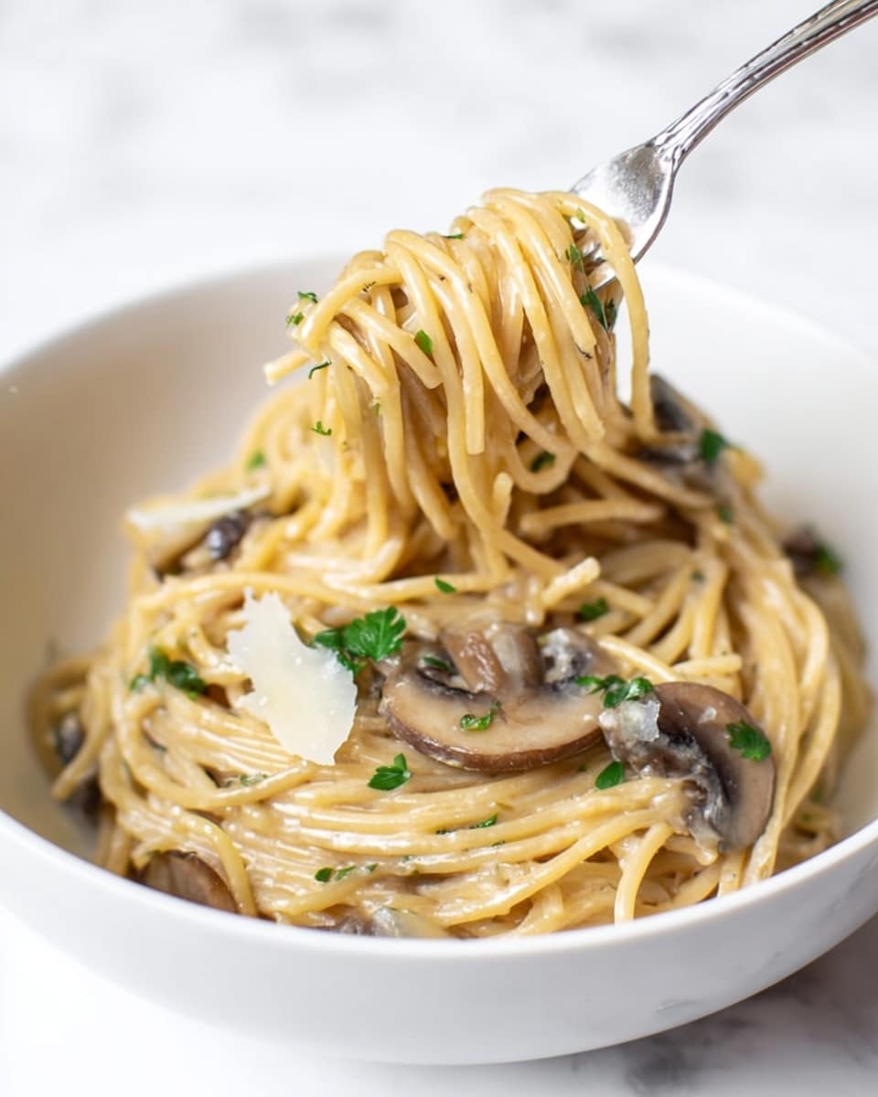A white bowl filled with creamy spaghetti shows a mix of light beige pasta strands coated in a smooth, shiny sauce. There are several slices of brown mushrooms spread throughout, adding a soft texture and color contrast. Small green parsley bits are sprinkled lightly over the top, along with thin shavings of pale cheese. A fork is lifting a twist of the spaghetti above the bowl, showing the glossy, creamy texture of the noodles. The bowl is placed on a white marbled surface. photo taken with an iphone --ar 4:5 --v 7
