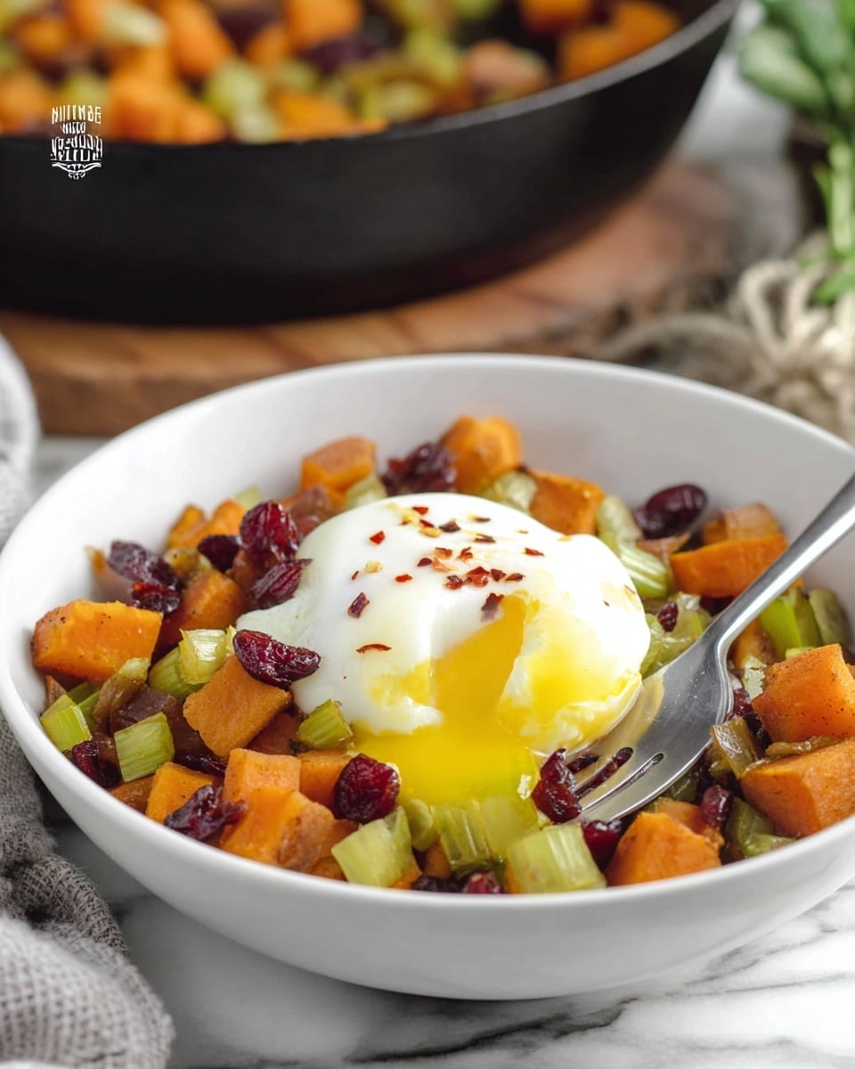 A white bowl filled with a colorful mix of diced orange sweet potatoes, light green celery slices, and dark red dried cranberries forms the base layer. On top of this is a perfectly poached egg with bright white, soft edges and a golden yellow yolk that is oozing out slightly. The egg is sprinkled with small, red chili flakes adding a touch of spicy detail. A silver fork rests on the right side inside the bowl, with a white marbled surface beneath it. In the blurred background, a black cast iron skillet with more of the same vegetable mix is visible. photo taken with an iphone --ar 4:5 --v 7
