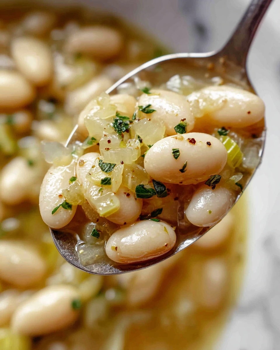 The image shows a close-up view of a spoonful of cooked white beans mixed with soft cooked celery pieces and small herb leaves. The white beans have a smooth, shiny surface, and the celery pieces are light green and translucent. The mixture is coated with a light broth or sauce with visible black pepper specks and small bits of herbs scattered around. The background is slightly blurred but shows the same bean and celery mix, emphasizing the texture and moisture of the dish. photo taken with an iphone --ar 4:5 --v 7