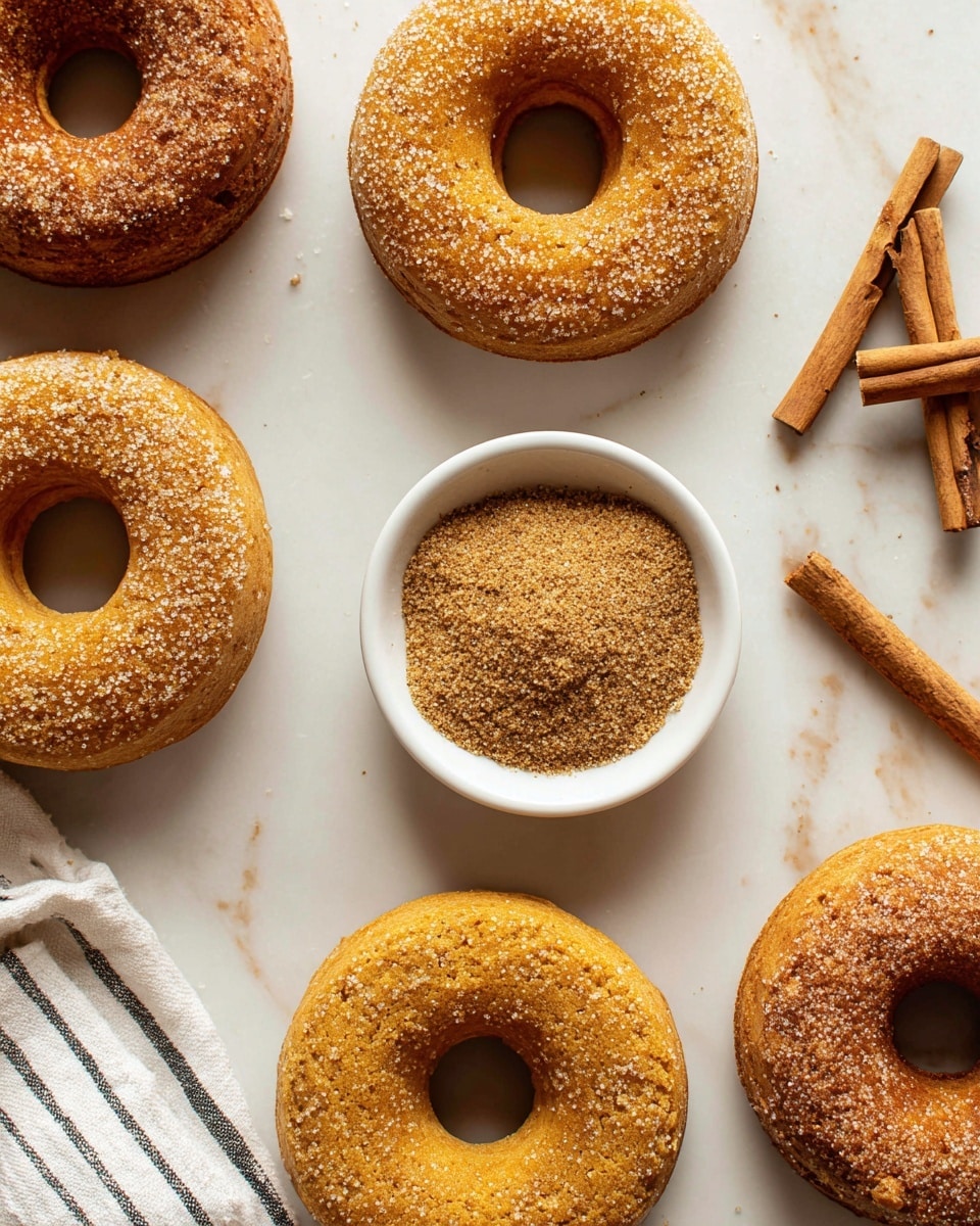 The image shows five round donuts with a golden brown color, covered with coarse sugar crystals on top. They are laid out on a white marbled surface with gaps between them. In the center, there is a small white bowl filled with finely ground cinnamon powder, with some cinnamon sticks placed diagonally at the top right corner of the image. A corner of a white cloth with black stripes is visible at the bottom left. The overall look is warm and inviting with the golden hues of the donuts and the rich brown of the cinnamon. photo taken with an iphone --ar 4:5 --v 7
