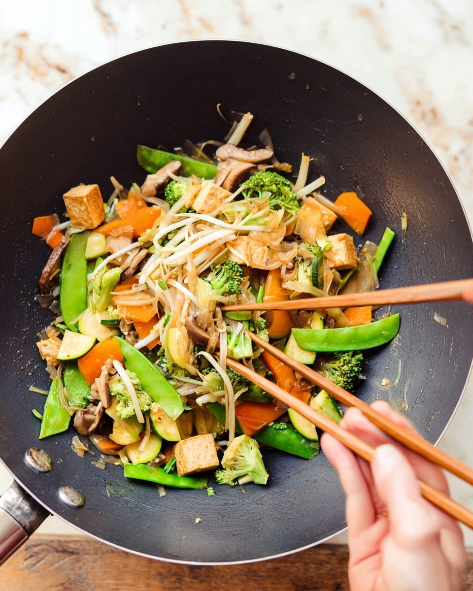 A close-up view inside a dark non-stick wok showing a colorful mix of stir-fried vegetables and tofu. The dish has about five layers: the bottom layer has chopped green broccoli and celery pieces with bright green snap peas; above it are sliced orange carrots and zucchini chunks with light brown tofu cubes scattered around. Thin white bean sprouts and light beige mushroom slices are mixed evenly throughout the dish. A woman's hand holding wooden chopsticks is picking up some of the stir-fry from the top. The wok is placed on a surface with a white marbled texture. photo taken with an iphone --ar 4:5 --v 7