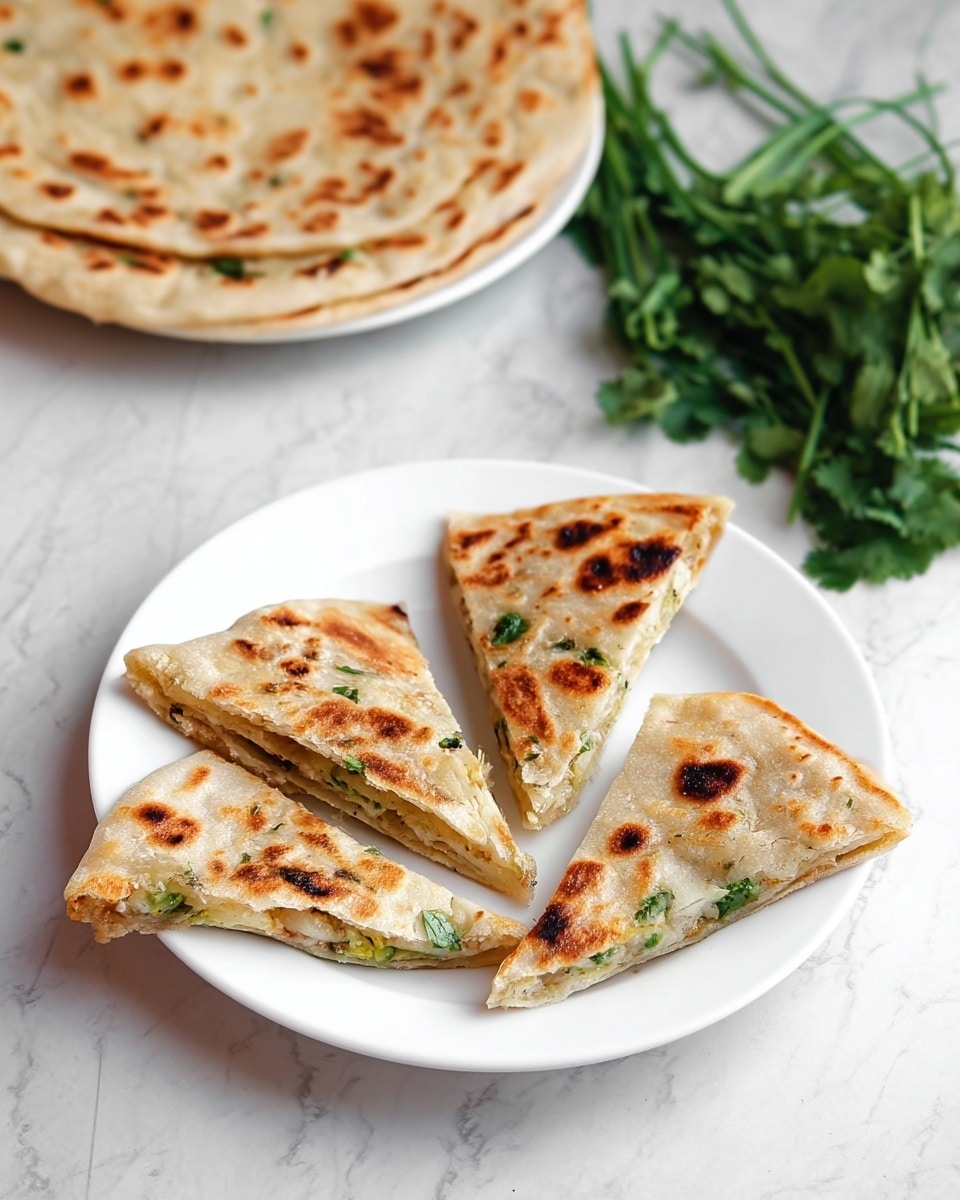 The image shows a white plate with four triangular pieces of stuffed flatbread that have a golden-brown, slightly charred surface with darker spots. Each piece reveals a visible layer of light filling inside, with a texture that looks soft and slightly crumbly, and some green herbs are visible in the filling. Behind this plate, there is another white plate with a whole flatbread of the same style, thick and round, featuring similar golden-brown spots and a slightly uneven edge. To the side, fresh green herbs are placed on a white marbled surface, adding a fresh contrast to the dish. Photo taken with an iphone --ar 4:5 --v 7