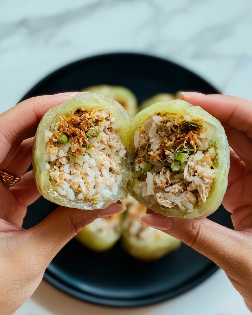 A close-up view of a food item held by two woman's hands, showing it cut in half to reveal its inside layers. The outermost layer is a translucent pale green vegetable skin that wraps the filling tightly. Inside, the filling has a mix of white rice grains and finely crumbled cooked tofu or meat with light brown and off-white colors, with some small green leafy herbs scattered throughout. The texture looks soft and moist, with a few crispy brown bits on the top edges. The black round plate below holds more pieces of the same food, slightly blurred, against a white marbled surface. Photo taken with an iphone --ar 4:5 --v 7